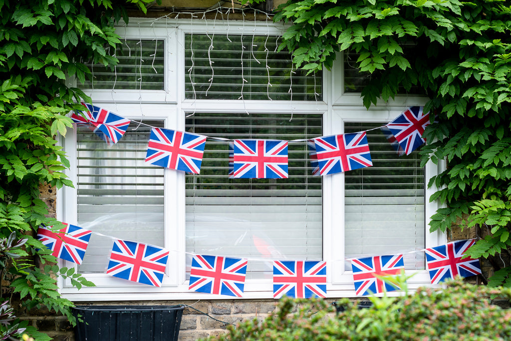 white paned window with blinds flag garland hangs over the window surrounded by ivy