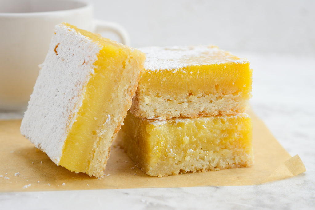 Two stacked lemon bars on brown parchment paper. A single lemon bar laid against the two sideways.