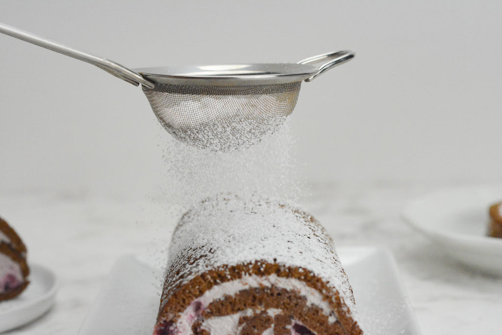 Icing sugar is dusted over the cake roll using a small fine mesh sieve