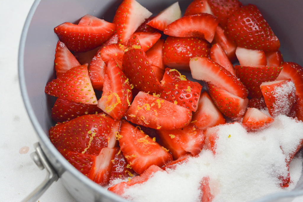 Close up of cut strawberries in a saucepan with sugar and lemon zest