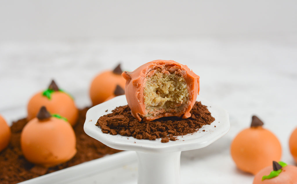 Pumpkin blondie truffles sit in graham cracker dirt to look like a pumpkin patch. A single pumpkin truffle sits towards the front on a cupcake stand with a bite taken out.