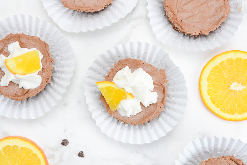 Mini cheesecakes sit inside of cupcake liners with large orange slices to the side