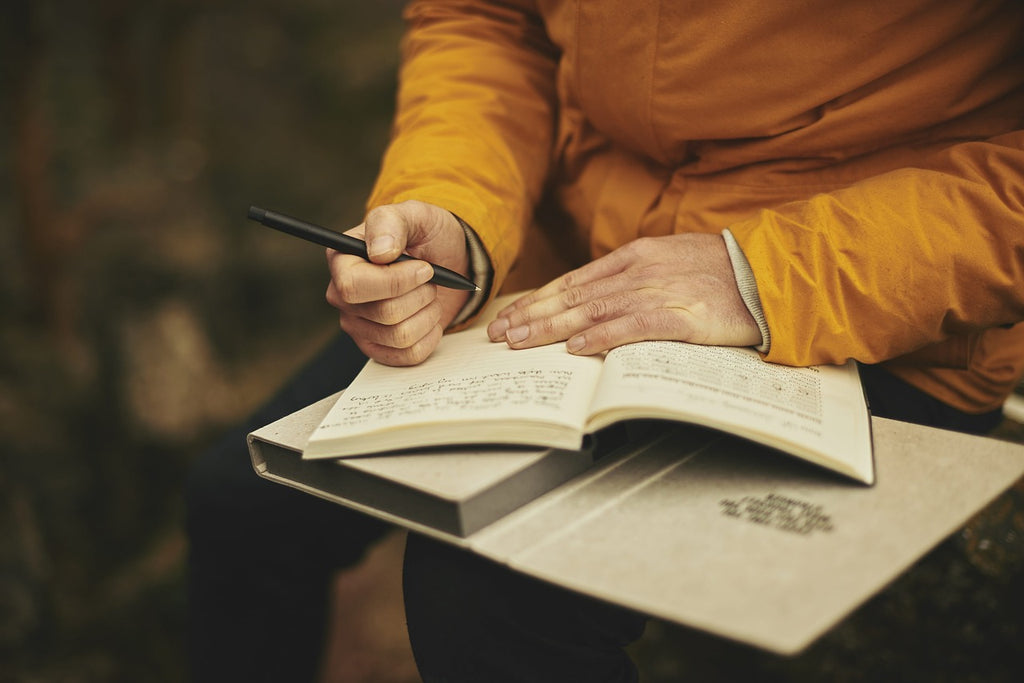 Adult in yellow jacket holds a small notebook and pen