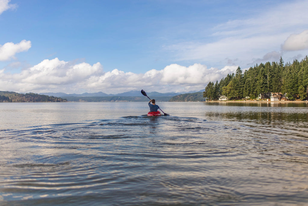 A canoe moves down a large open lake on a partly cloud days with green trees to the right