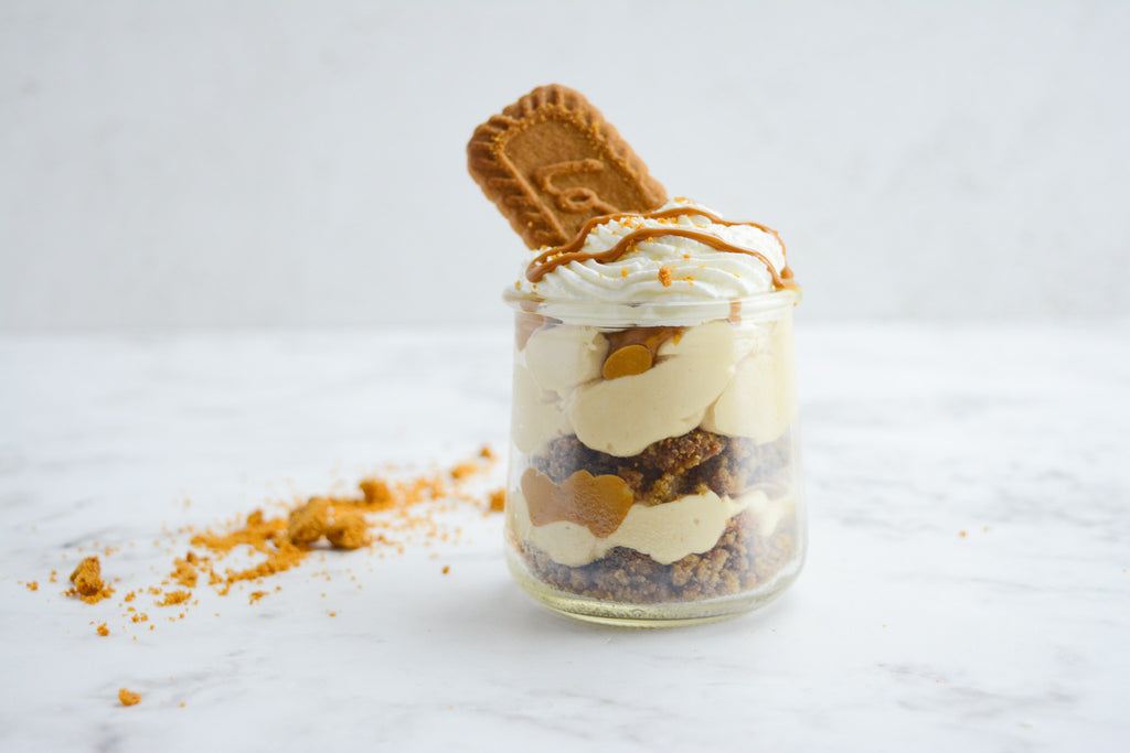 Single layered cheesecake cup sits on marble table top. Cookie crumbs scatter to the left of the cup and a single cookie sticks out of the top of the jar. 