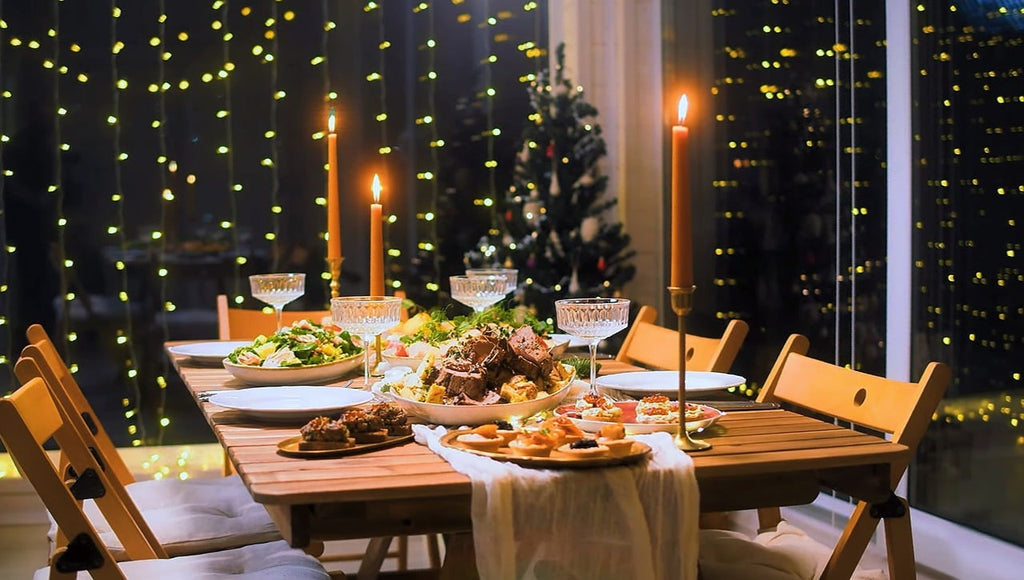Table set with food, please and tall red candles. Strings of lights decorate the wall