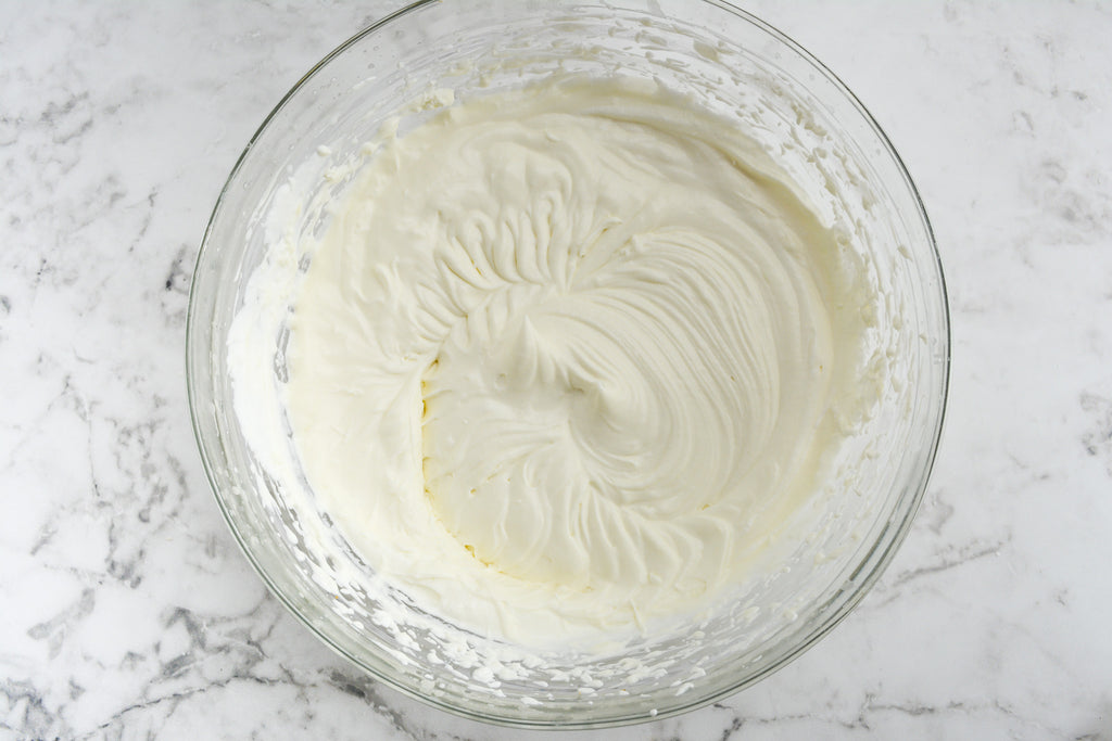 A large bowl on a marble surface is filled with whipped cream