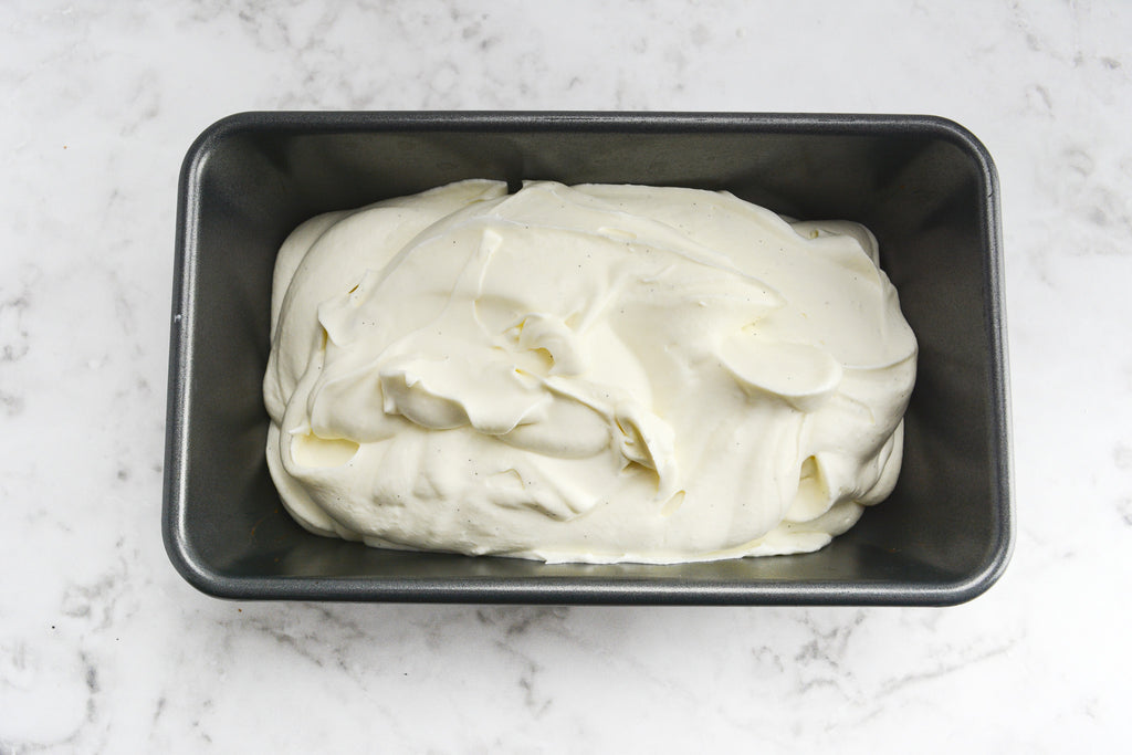 A silver pan of ice cream sits on a marble surface. The white ice cream is swirled after being scraped into the pan