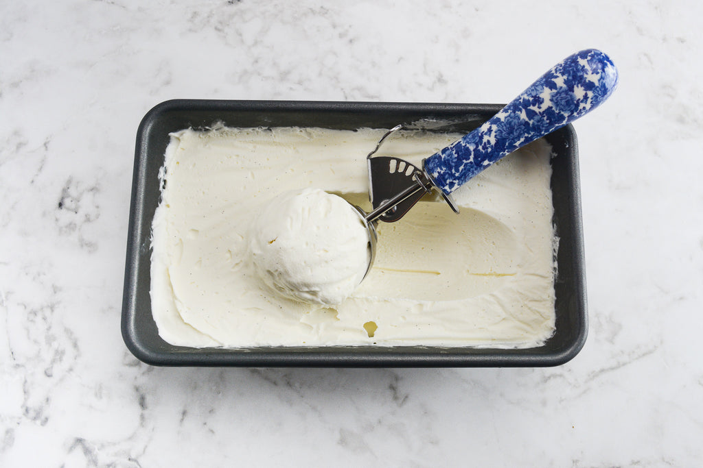 Silver loaf pan filled with white ice cream. A blue and white ice cream scoop sits in the center filled with a round scoop of ice cream.