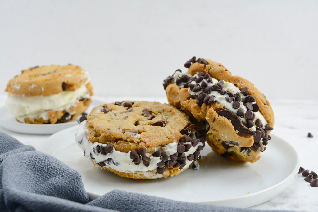 Three ice cream sandwiches sit on a white plate. Two are stacked while a third sits behind them