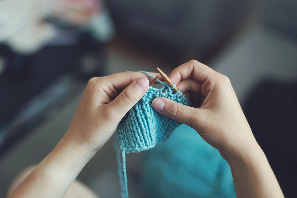 Hands knitting a medium blue scarf