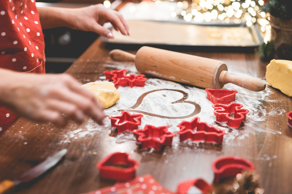 Person draws a heart in flour next to red Christmas cookie cutters. A rolling pin sits to the side.