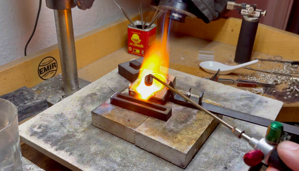 A crucible with melted gold at the verge of being poured into a graphite ingot mold, capturing the decisive moment.