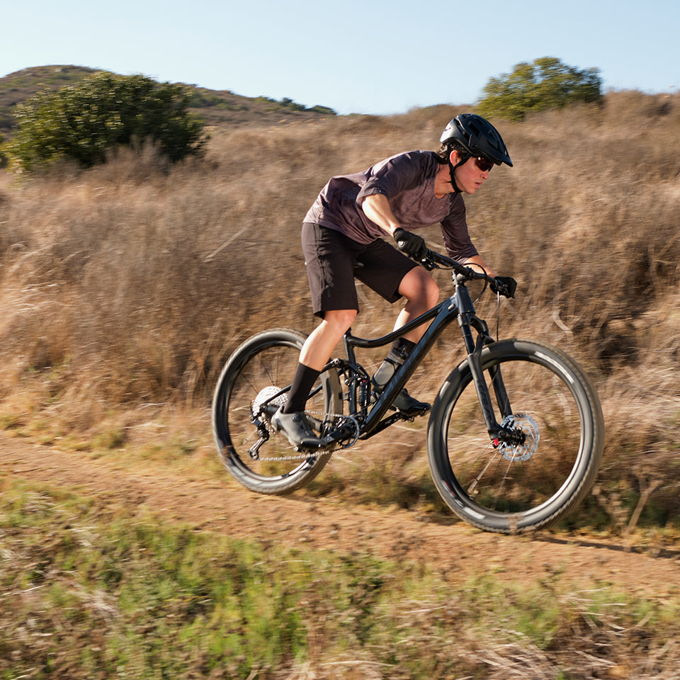Man rides his giant mountain bike through a dirt trail against a backdrop of hills