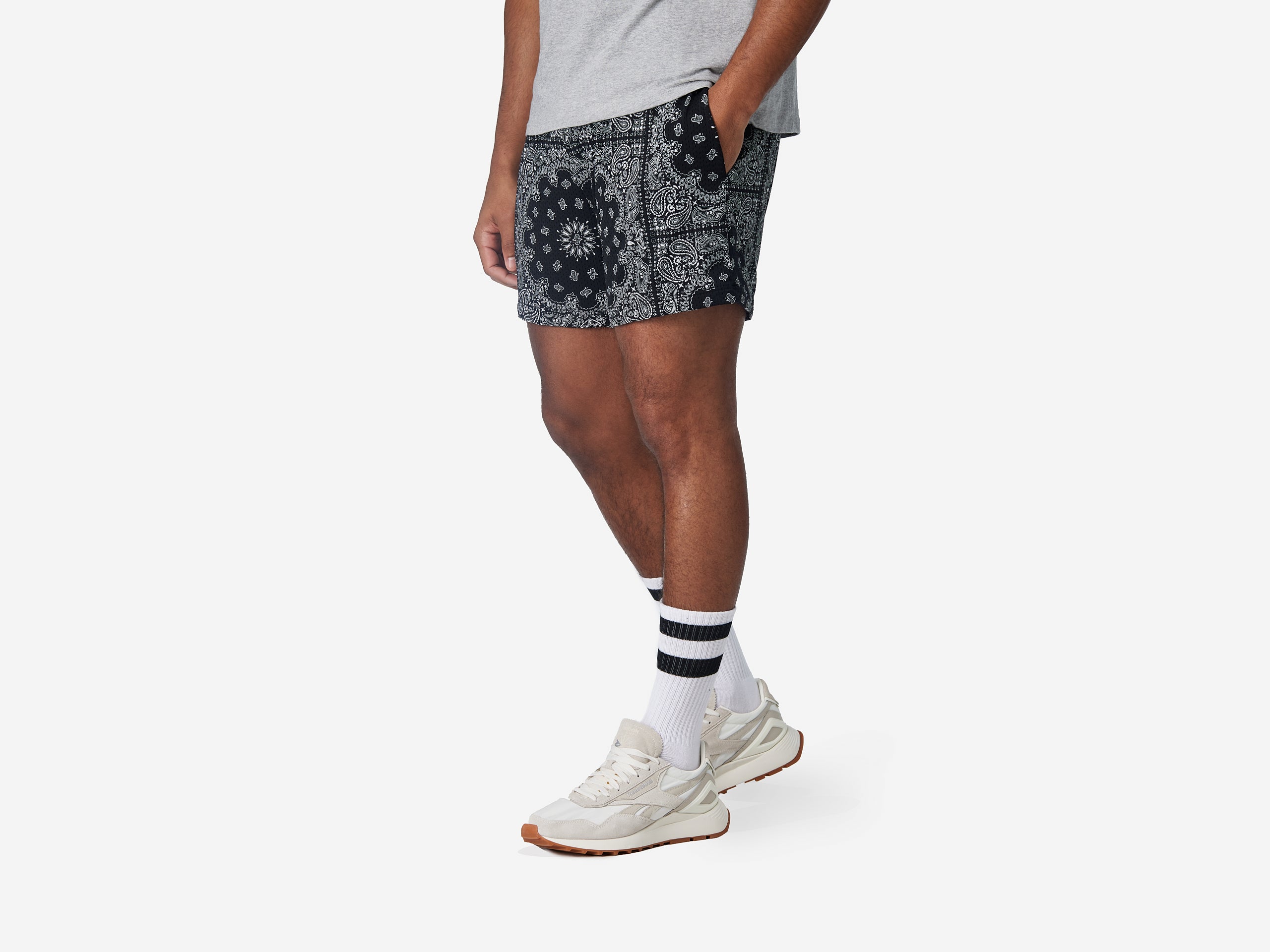 Man wearing black bandana print mesh shorts with hand in pocket