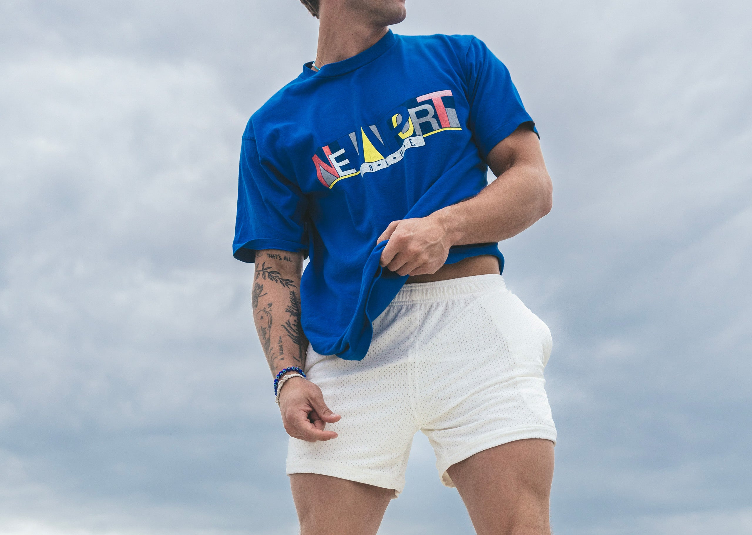 Man wearing blue shirt and cream colored lounge shorts with blue sky behind him.