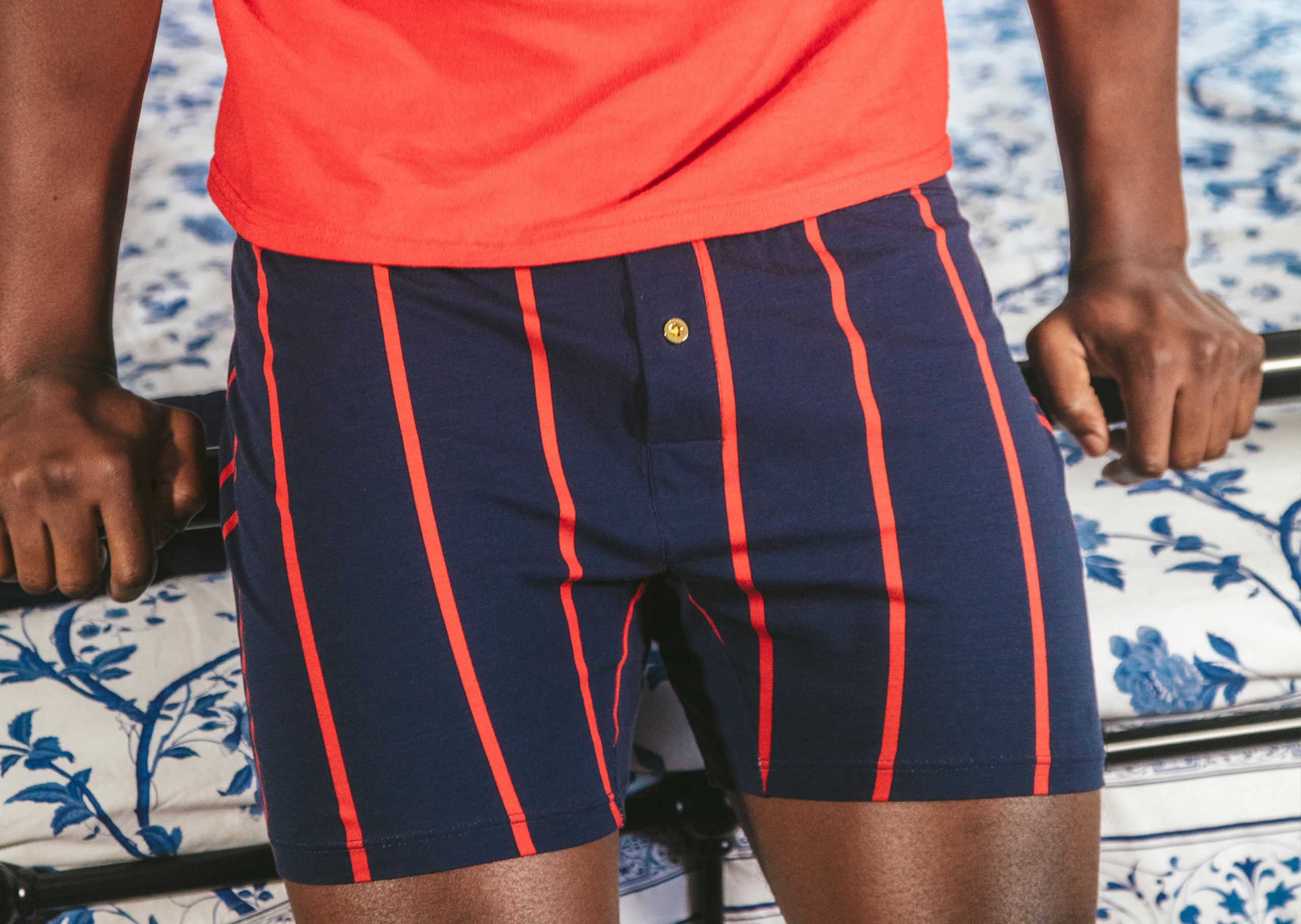 Close up of man leaning on bed railing wearing blue and red stripe Mariner slim fit boxer.