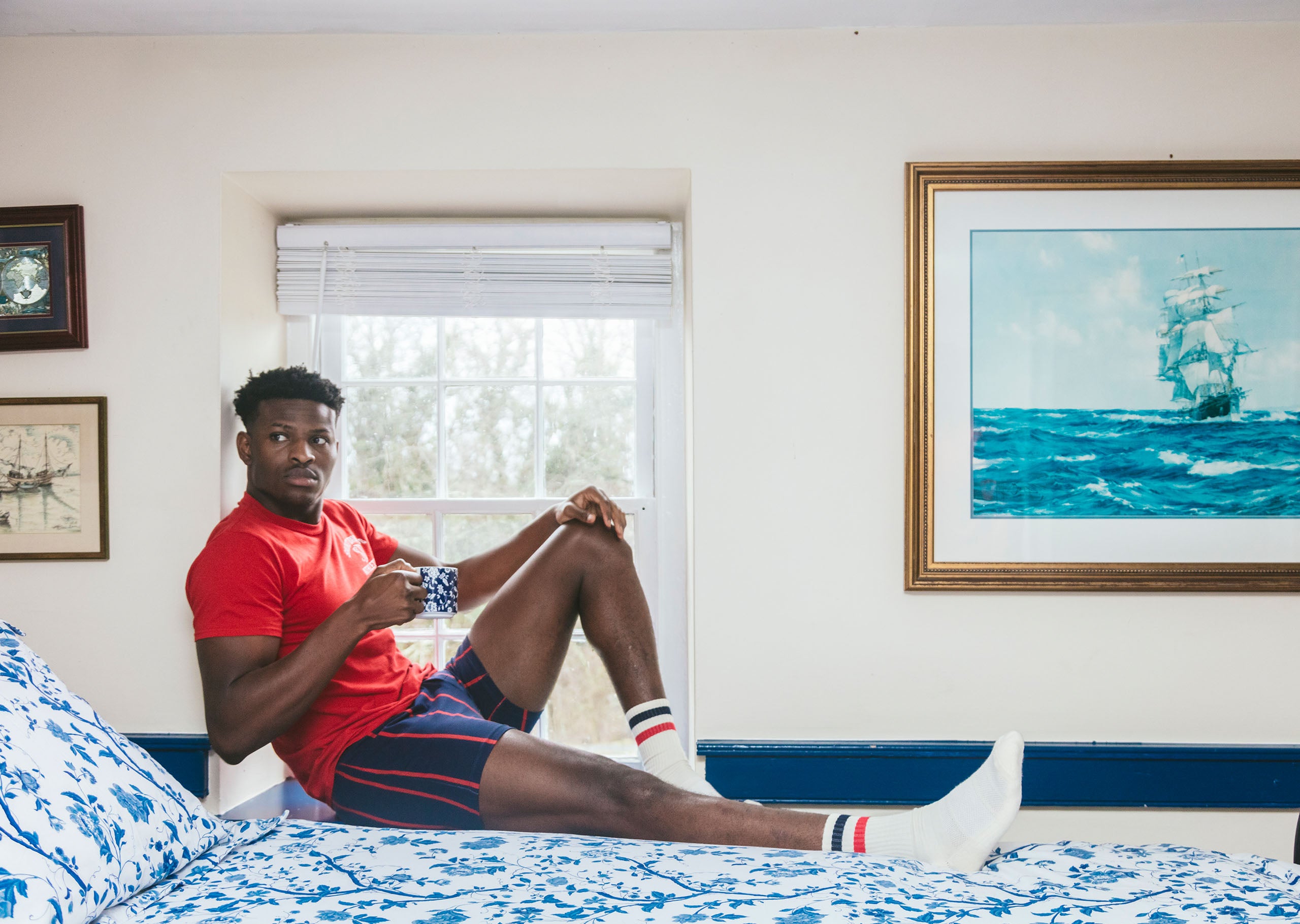 Man laying on blue bed holding a tea cup wearing red white and red/blue stripped slim fit boxer.