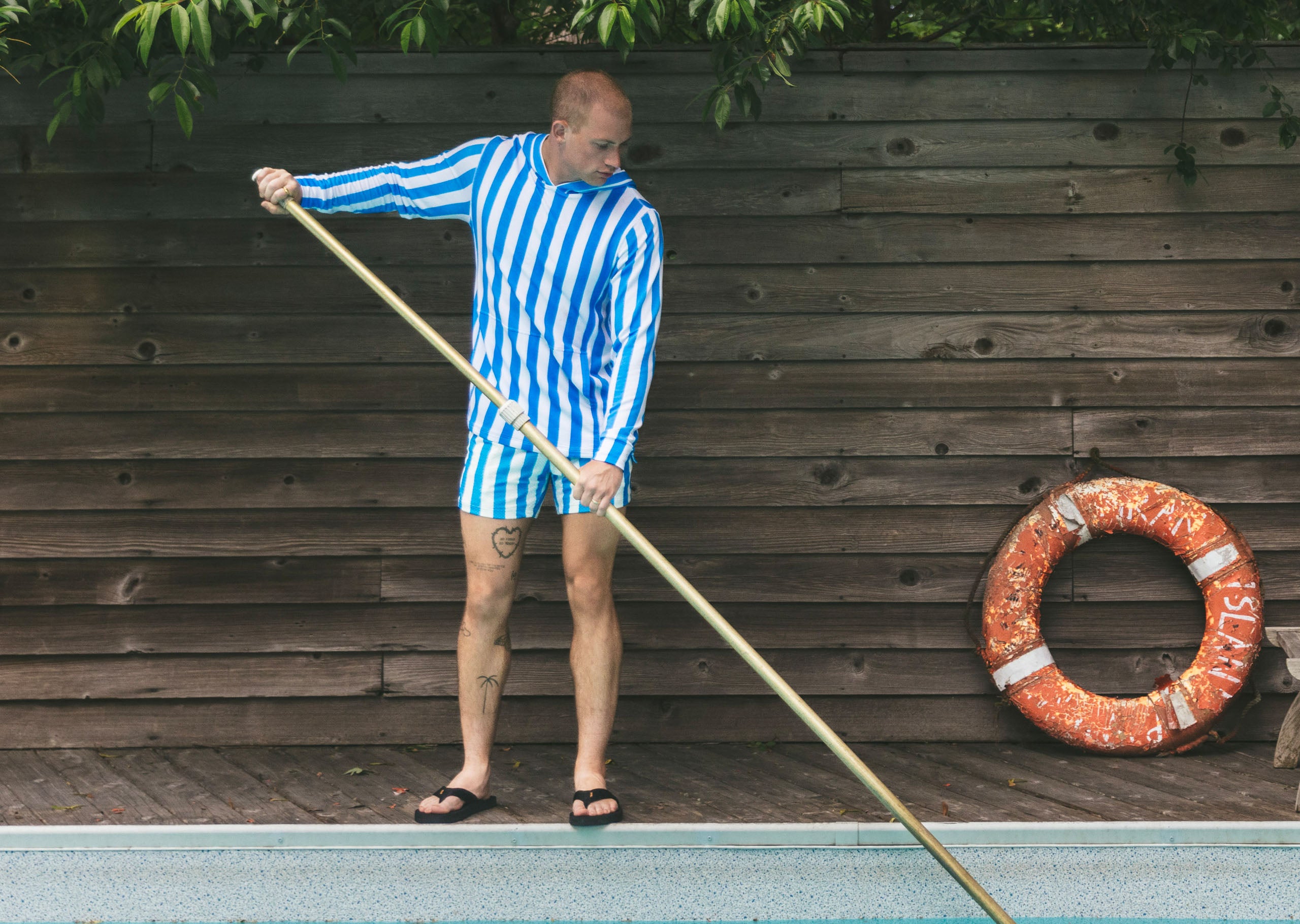 Man cleaning pool wearing blue and white stripped hoodie and shorts.
