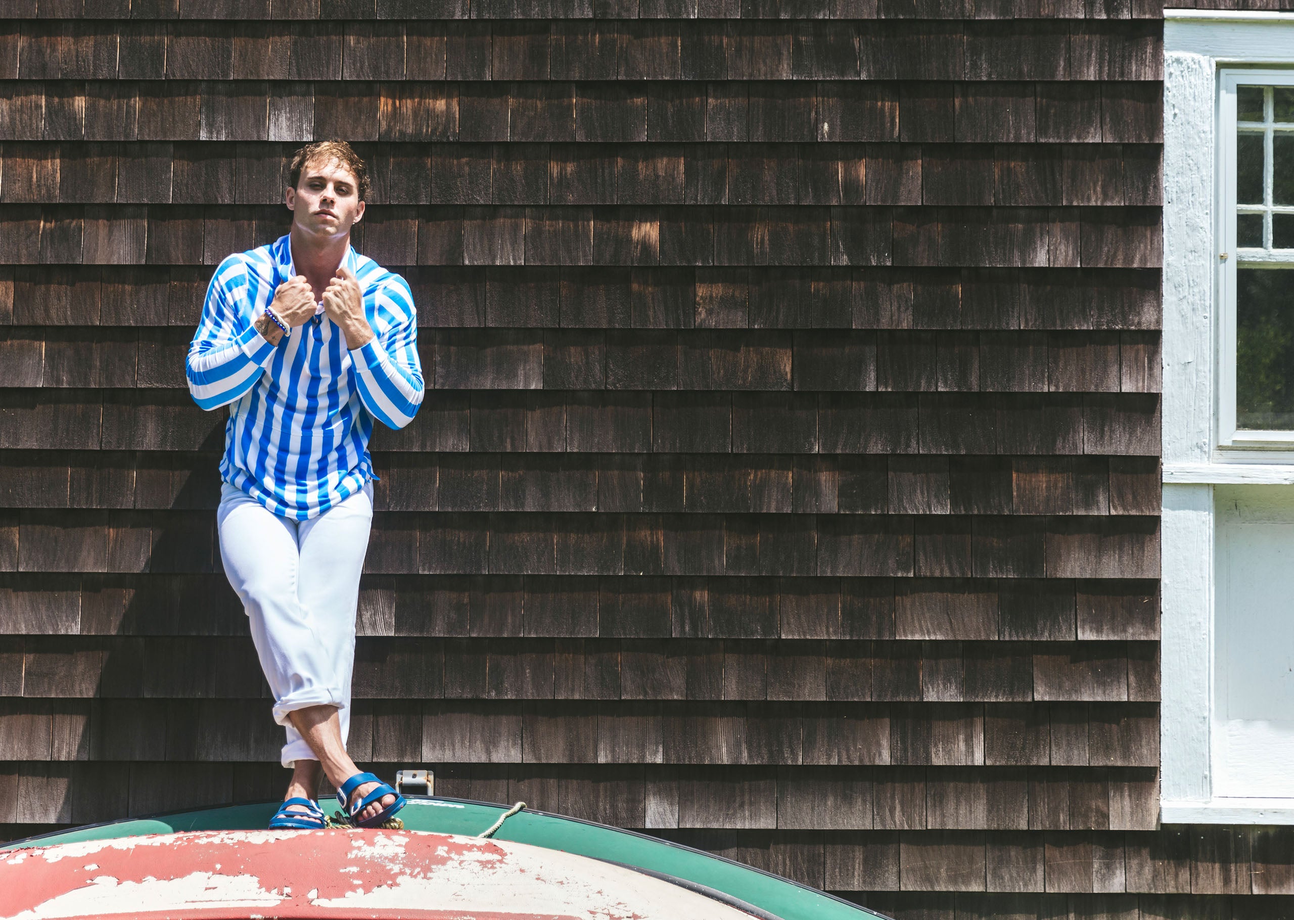 Man standing by house roof wearing blue and white stripe cabana hoodie.