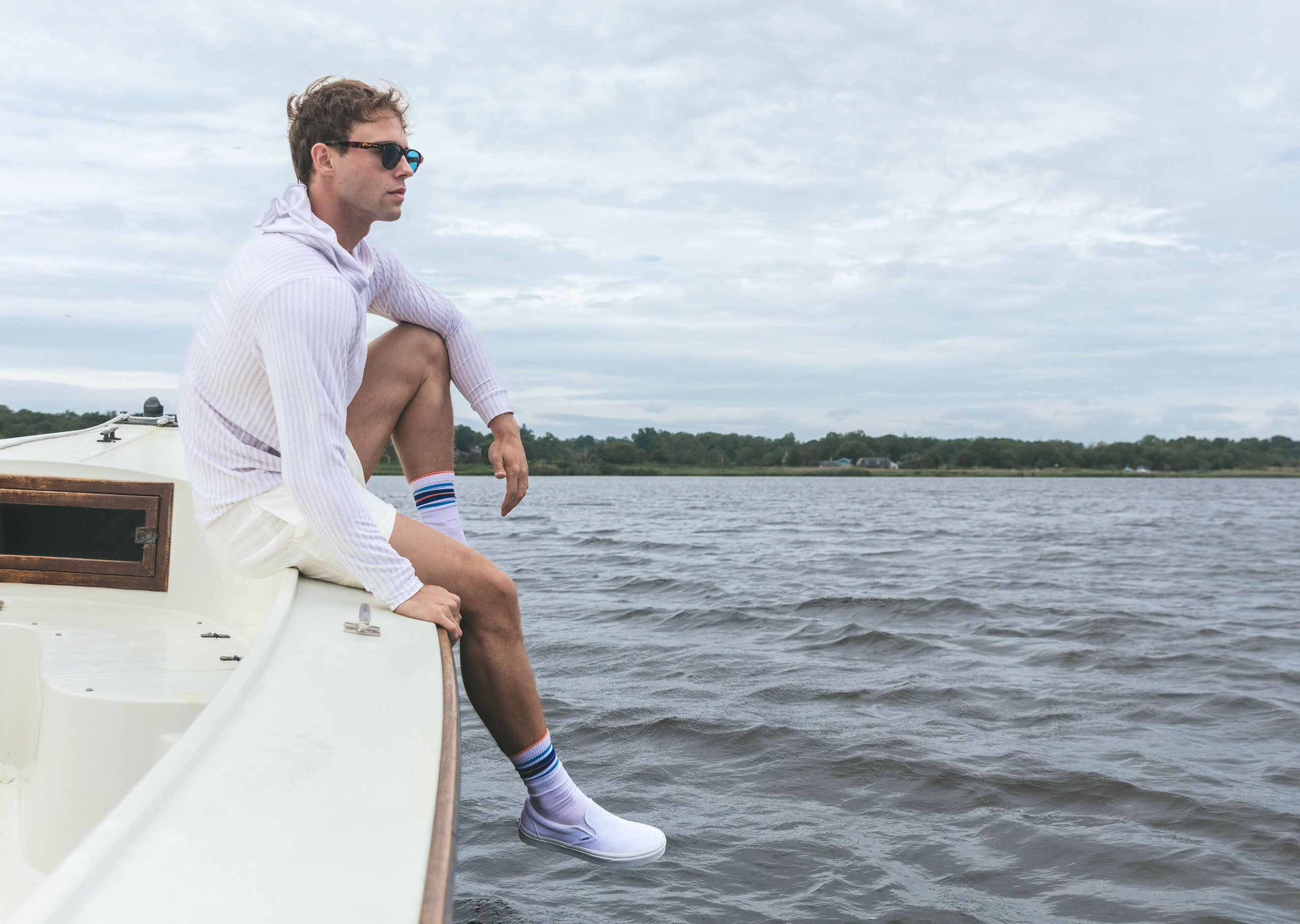 Man sitting at the edge of a boat wearing a linen stripe hoodie.