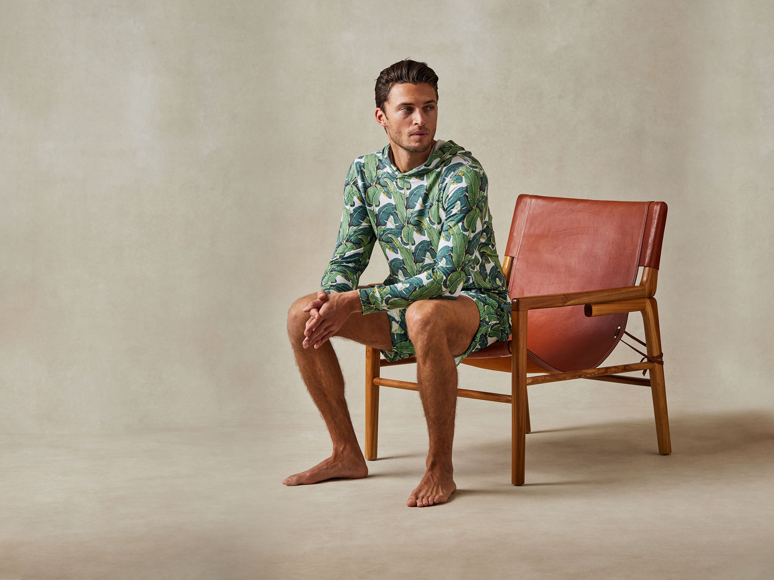 Man sitting in chair wearing palm print lounge hoodie and shorts.