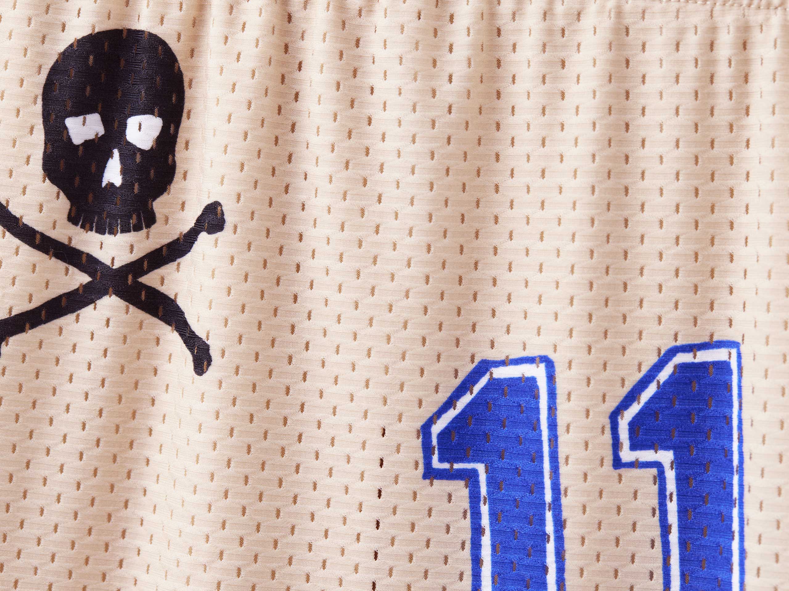 Close up detail shot of beige senior cord mesh lounge short. Black skull and blue "11" visible.