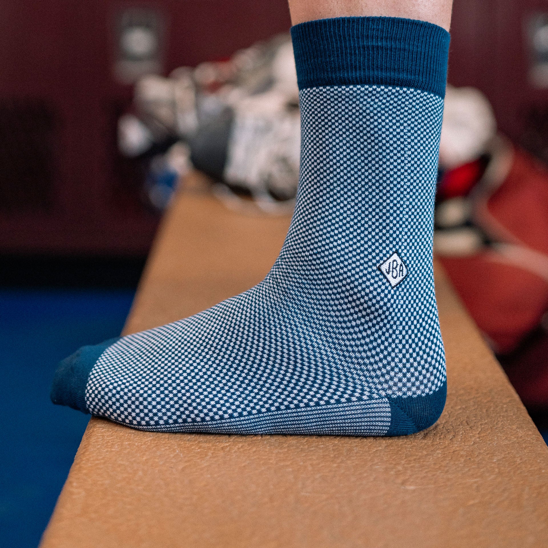 Close up shot of man's foot wearing blue Birdseye printed dress socks with initials "JBA" monogrammed on them.