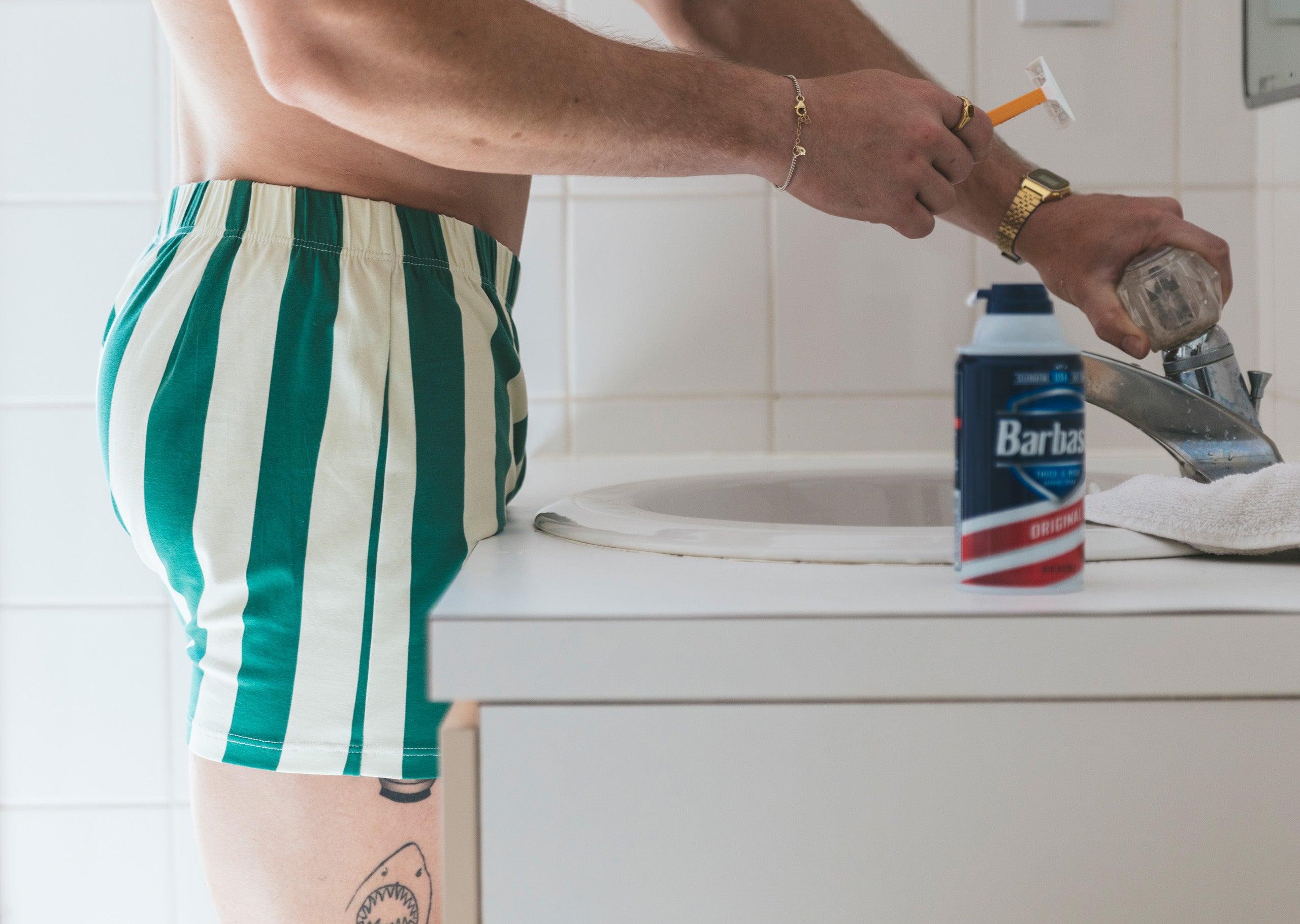 Man standing shirtless in bathroom at sink shaving wearing hunter green and cream stripe slim fit boxer.