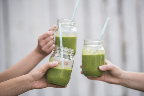 Three people clinking their glasses of green smoothies