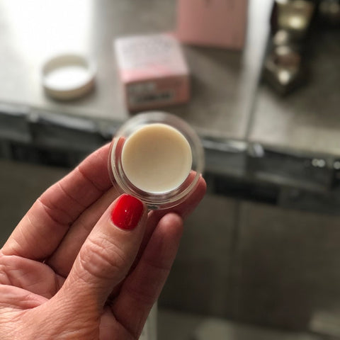 A person holding a small jar of lip balm