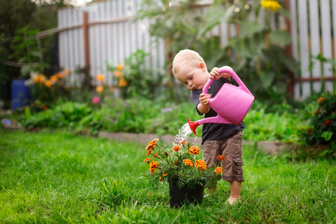 toddler learning how to water plants outside by gardening