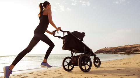 Woman Running On The Beach With A Jogger Baby Stroller