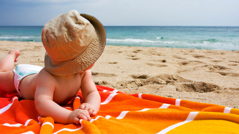 baby sitting on a towel with a hat on the beach