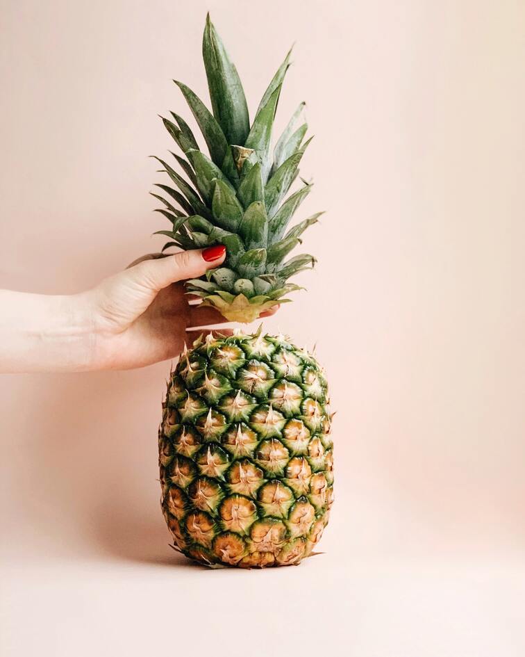 Ananas vor rosa Hintergrund, der Schopf abgeschnitten in einer Hand