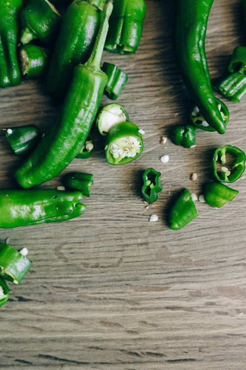 Grüne Chilis auf einem Holzbrett, teils aufgeschnitten, die weissen Samen verstreut