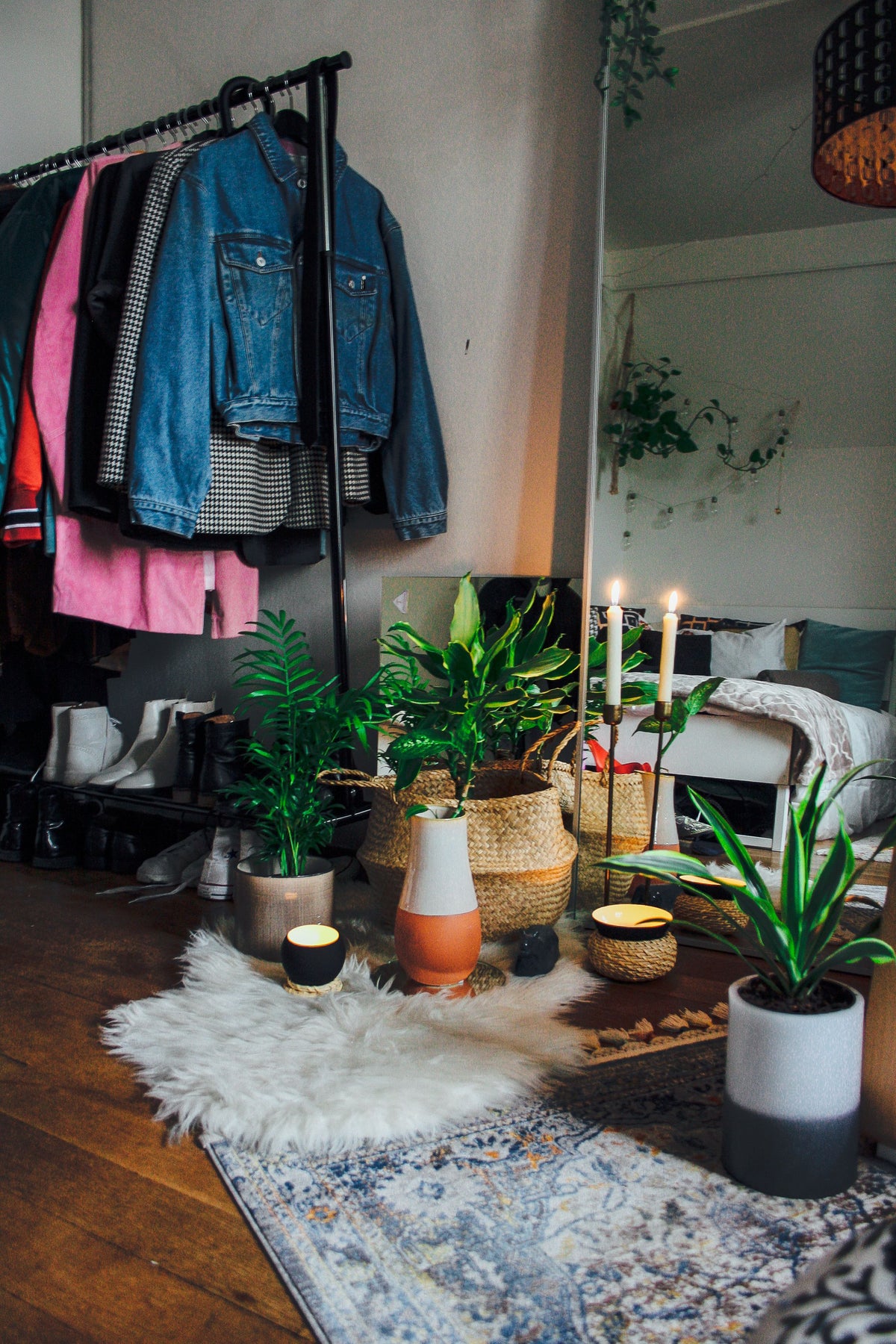 Ein buntes Zimmer mit vielen Pflanzen in verschiedenen Töpfen. Man sieht eine Kleiderstangeu nd zwei brennende Kerzen.