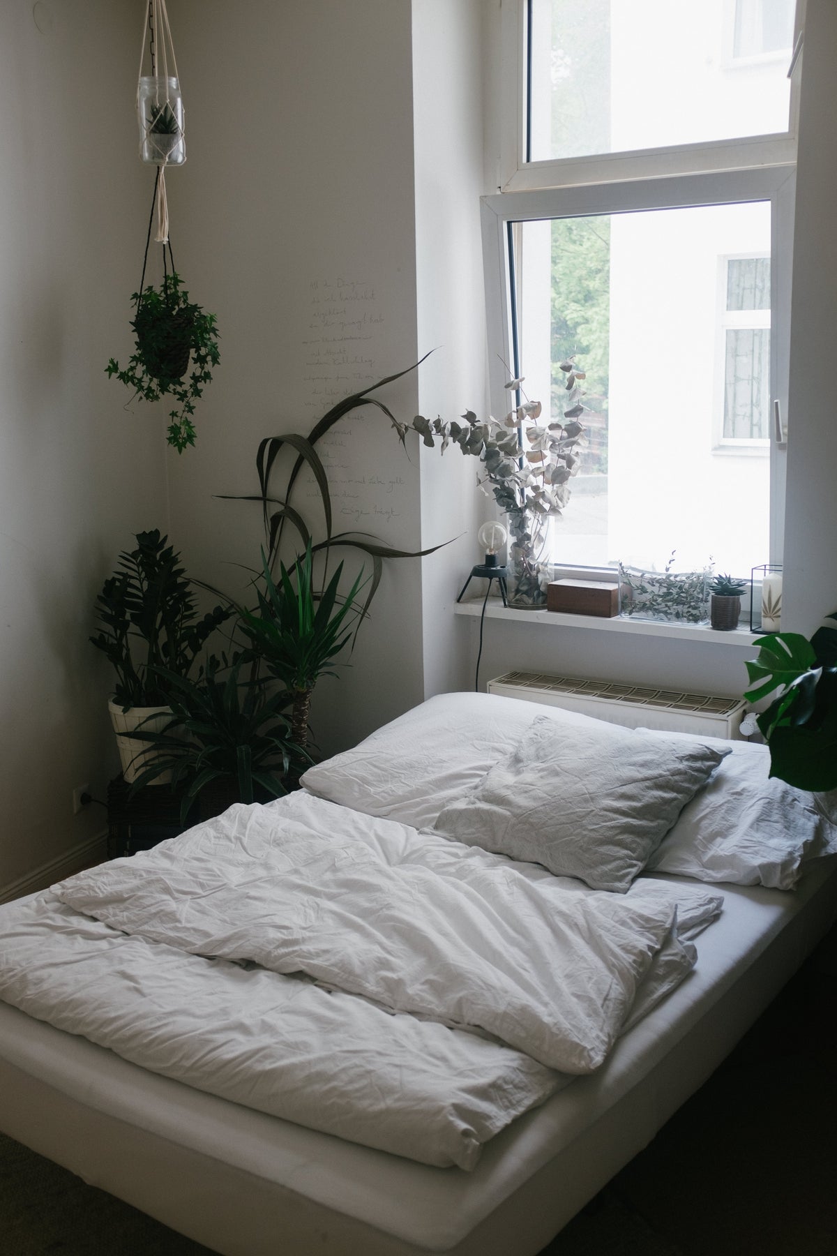 Minimalistisch eingerichtetes Schlafzimmer mit vielen Pflanzen. Die Bettwäsche ist weiss.
