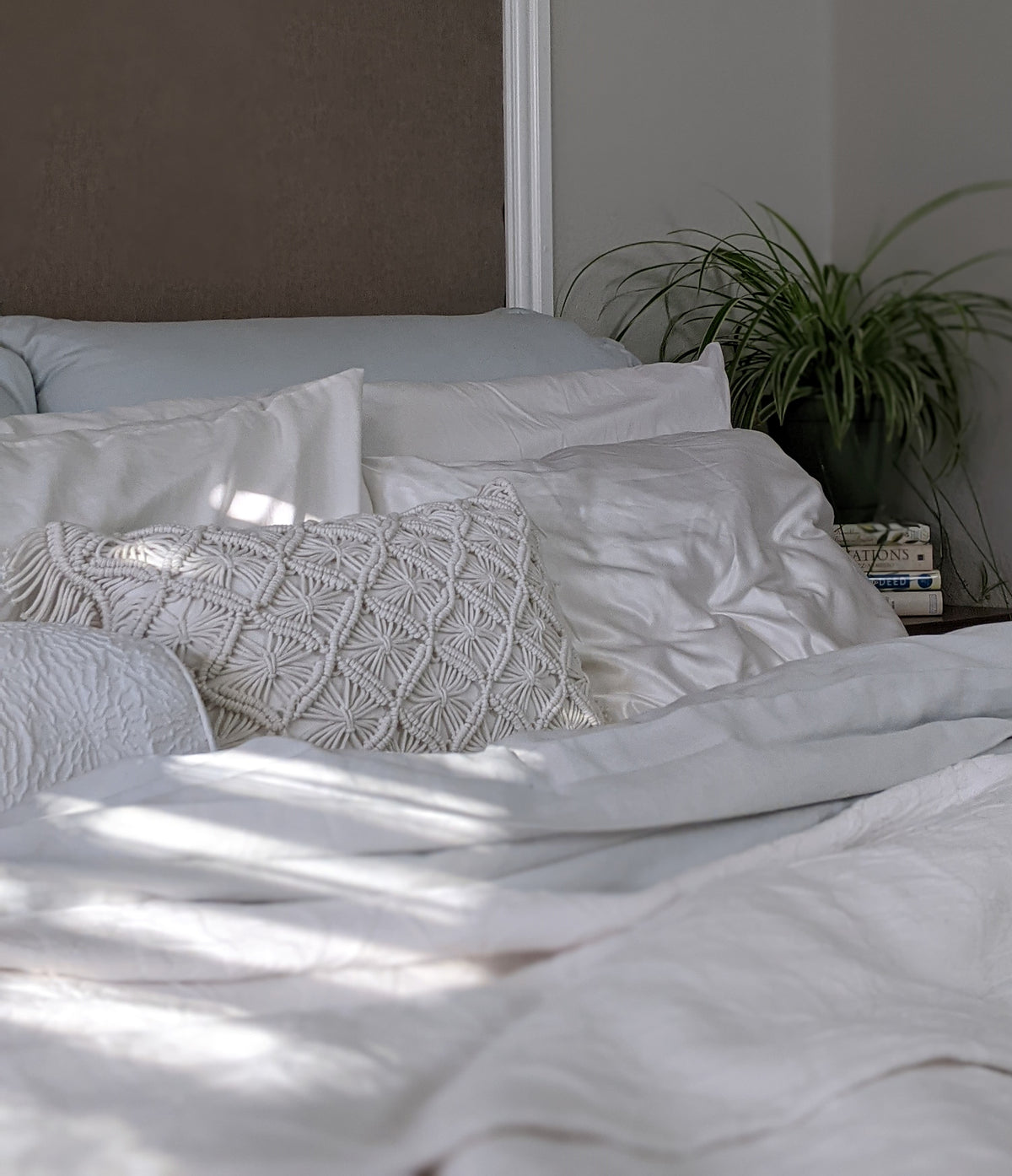 Ein Bett mit weisser Bettwäsche. In der Ecke auf dem Nachttisch steht eine Grünlilie.