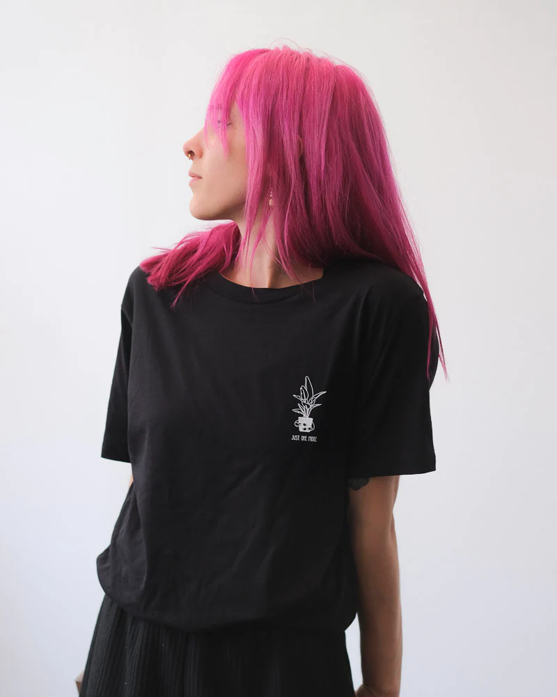 Frau mit pinken Haaren präsentiert ein schwarzes T-Shirt mit weissem Pflanzen-Aufdruck