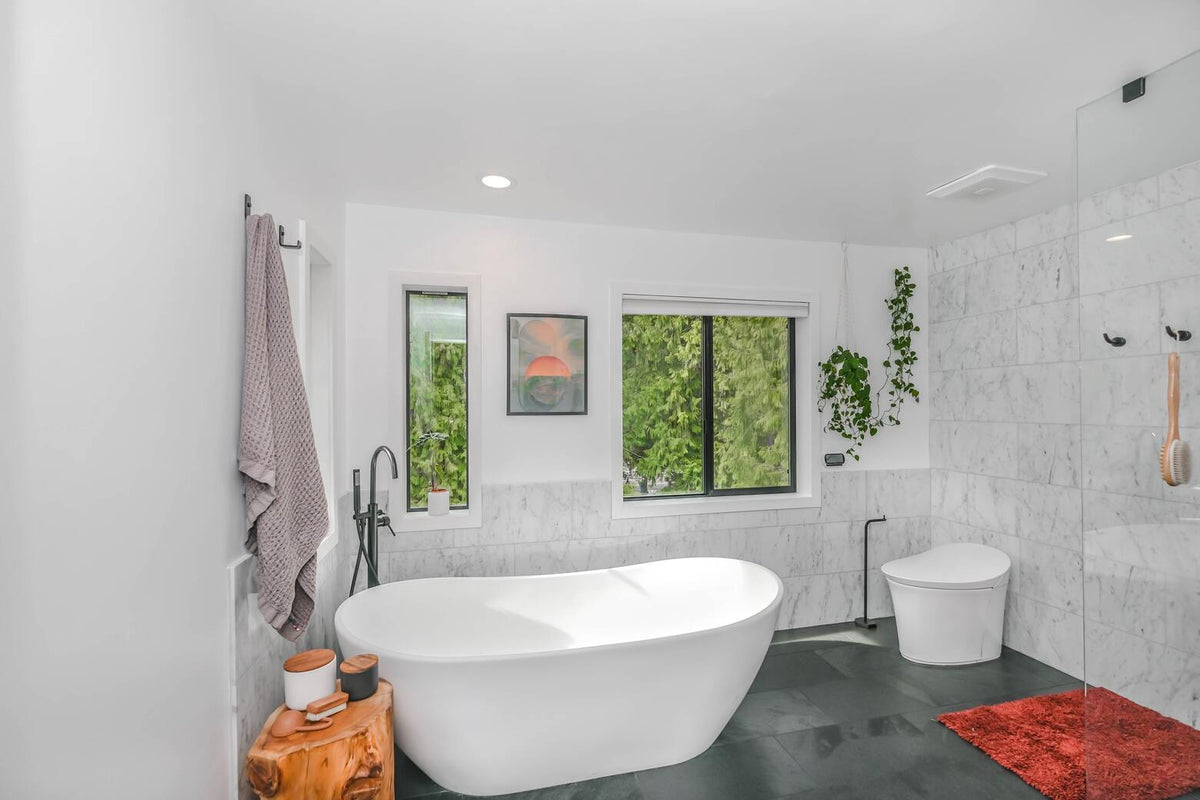 Weisses Bad mit dunkelgrauem Boden, freistehender Badewanne und einigen Hängepflanzen an den Wänden