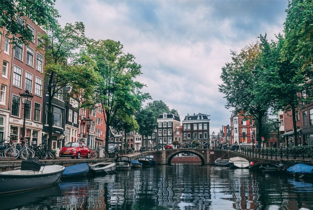 A popular canal in Amsterdam showing tree-lined streets, cars and boats.