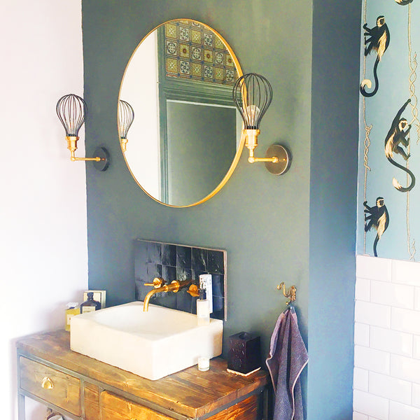 Green bathroom interior with two brass wall lights either side of a oval mirror