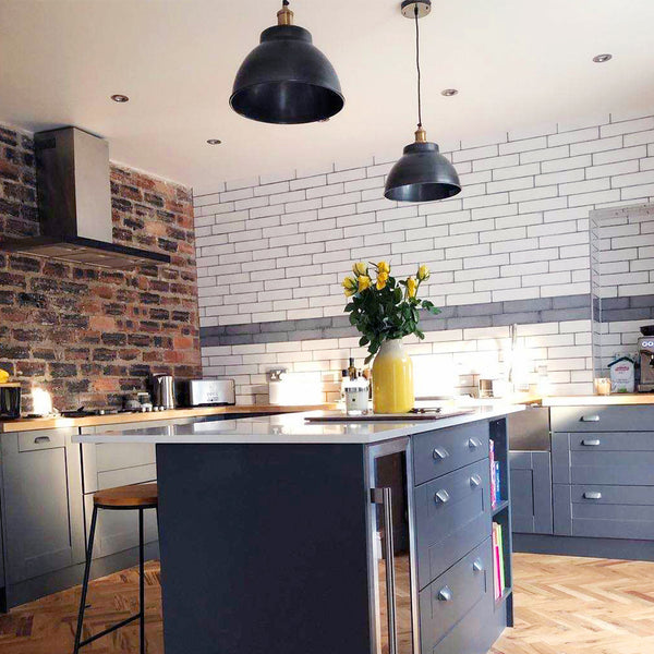 Industrial kitchen interior with exposed brick wall and duo of industrial lights above a kitchen island