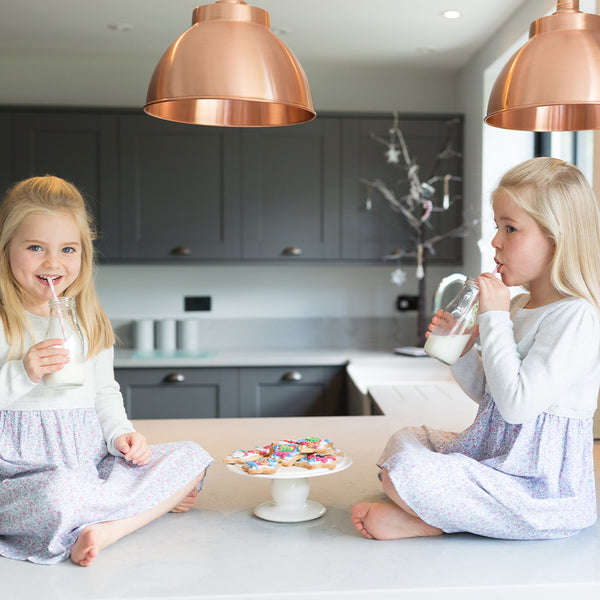 Twin girls drinking milk on kitchen counter with industrial pendants