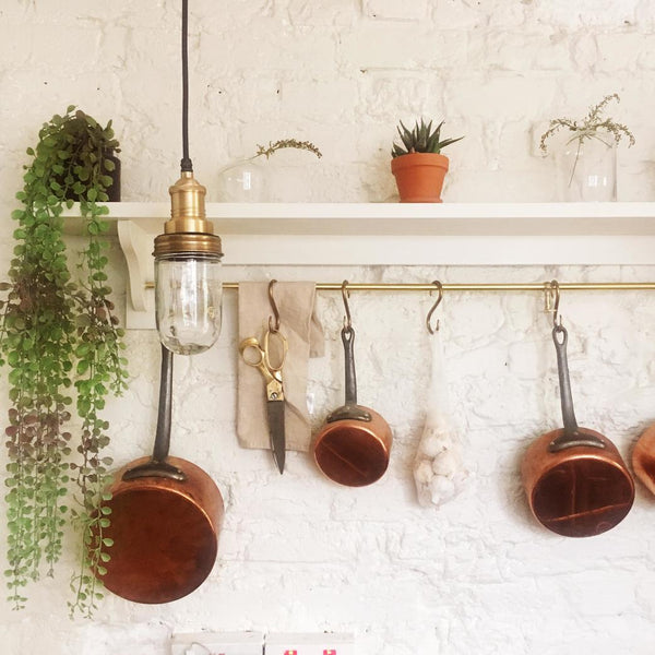 An exposed bulb pendant hanging in front of a shelf and rail of pots