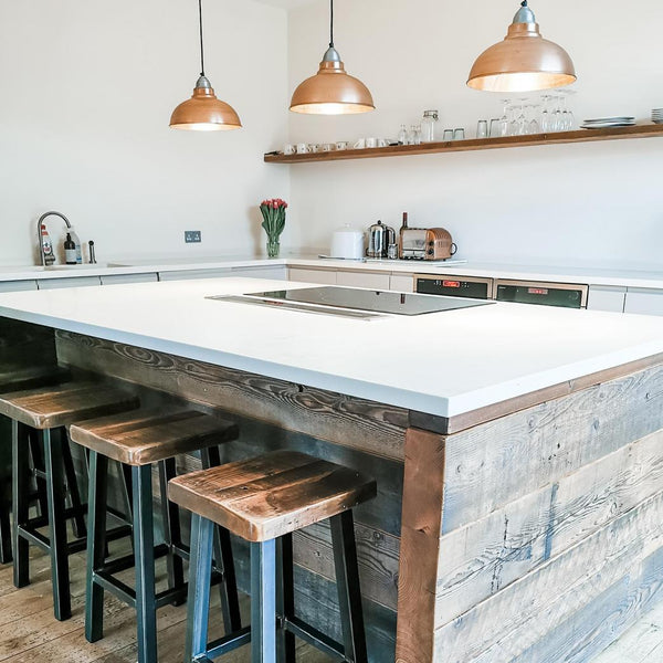 Three pendant lights hanging over a kitchen island and wooden stools