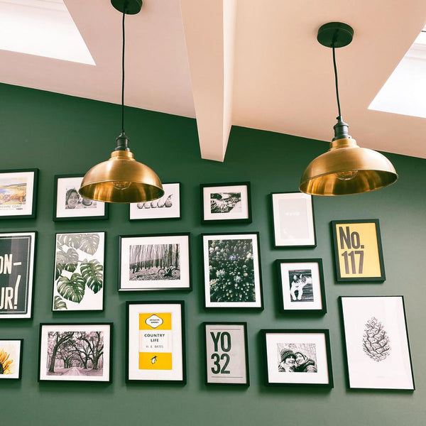 A gallery wall displayed on a green-painted wall with gold pendant lights