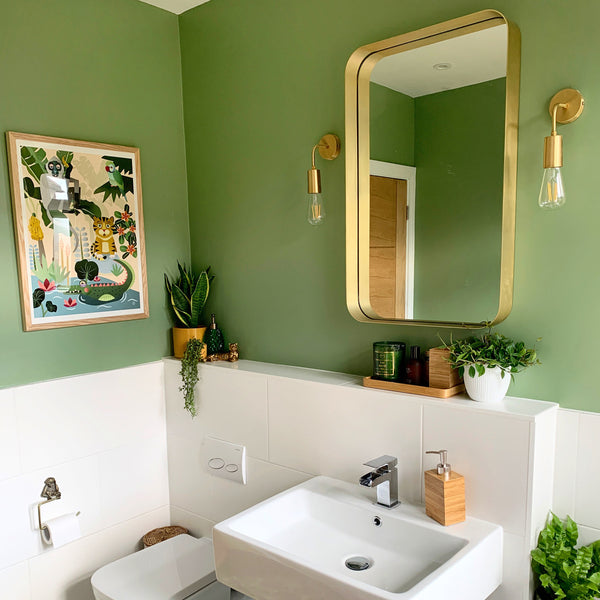 A brass Edison-style wall light in a green bathroom