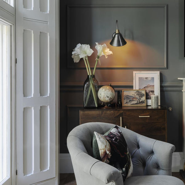 An armchair by a window and lit by a wall light